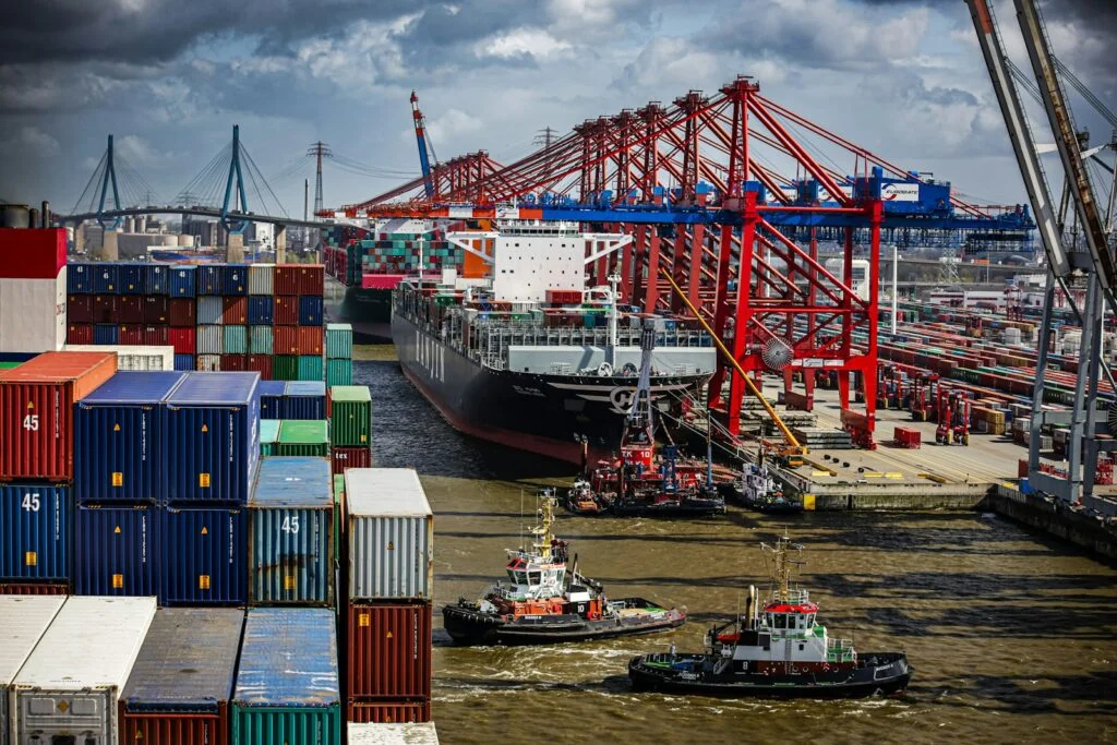 Container ship guided by tugboats past the cranes of a container terminal